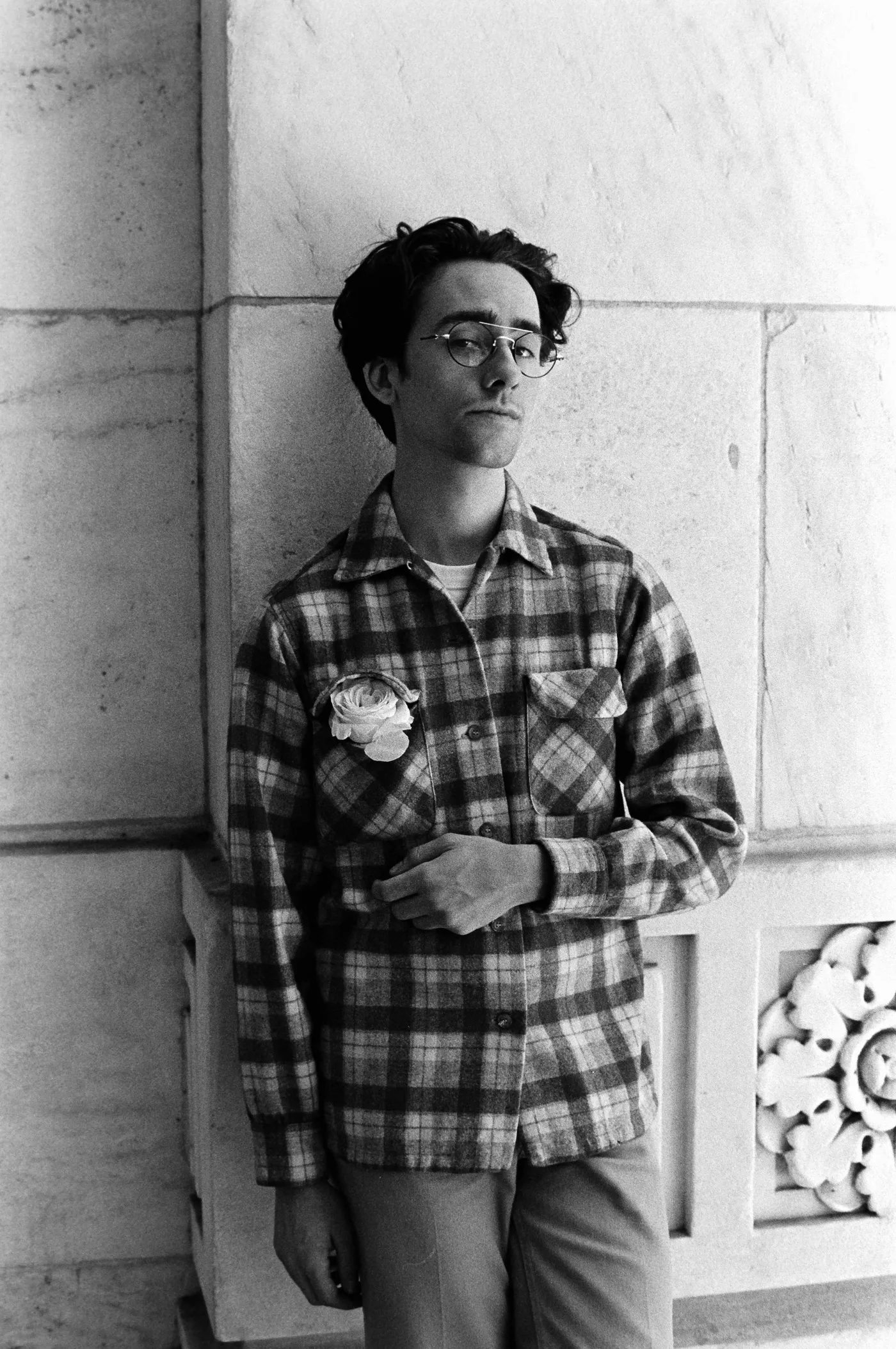 Black-and-white portrait of Tyler wearing glasses and a plaid shirt with a flower pinned to the pocket.