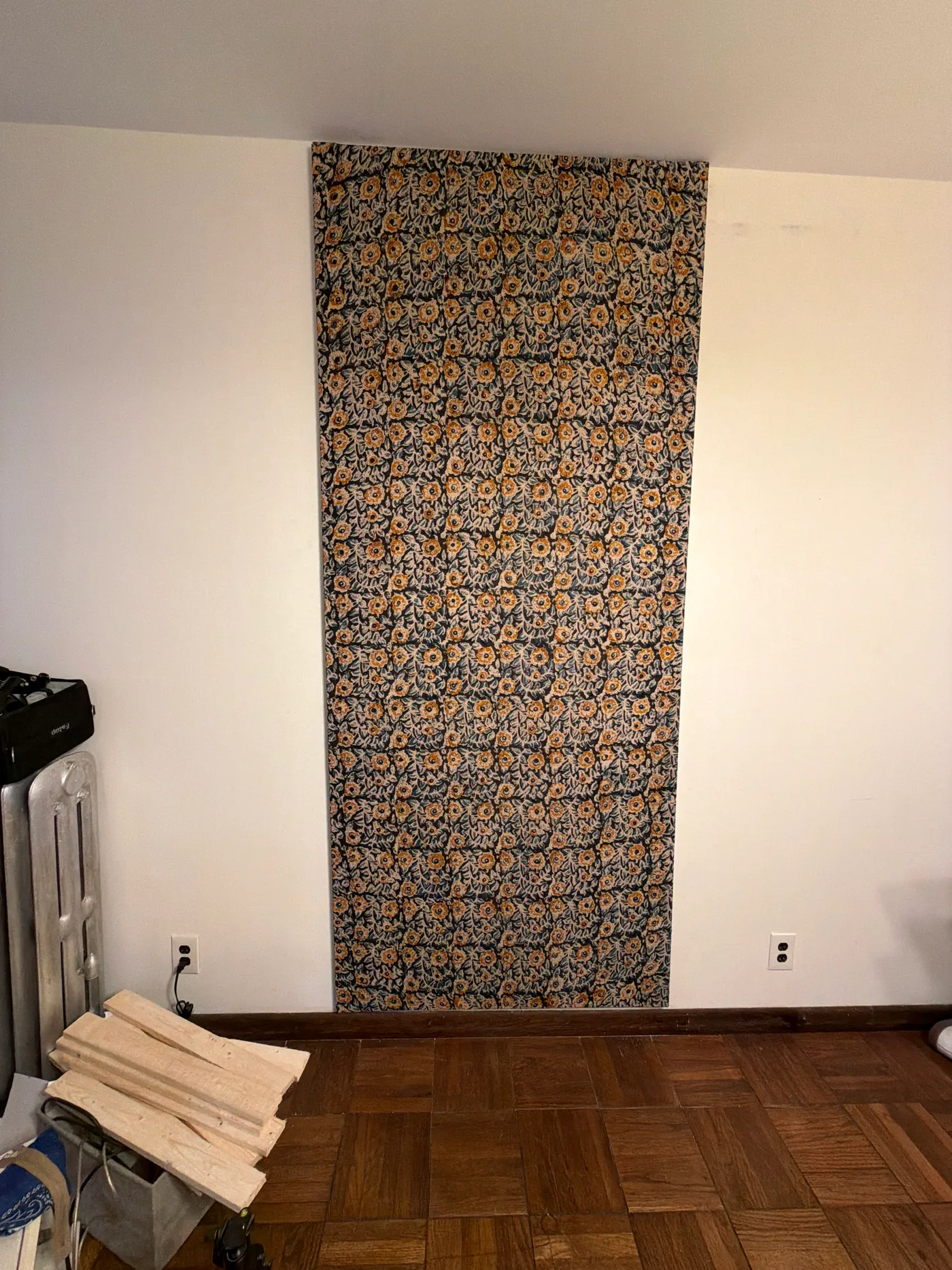 A dark floral patterned textile hanging on a wall above a wood floor