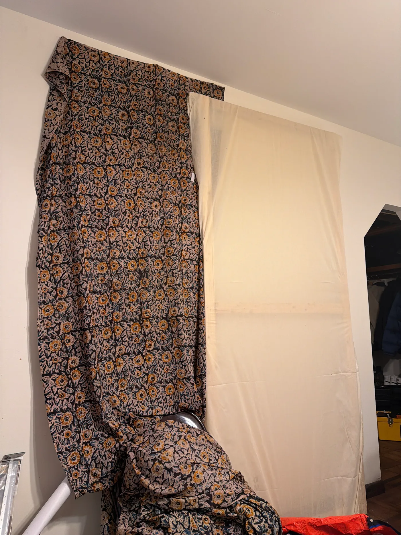 A dark floral patterned textile hanging beside a plain cream-colored fabric panel indoors