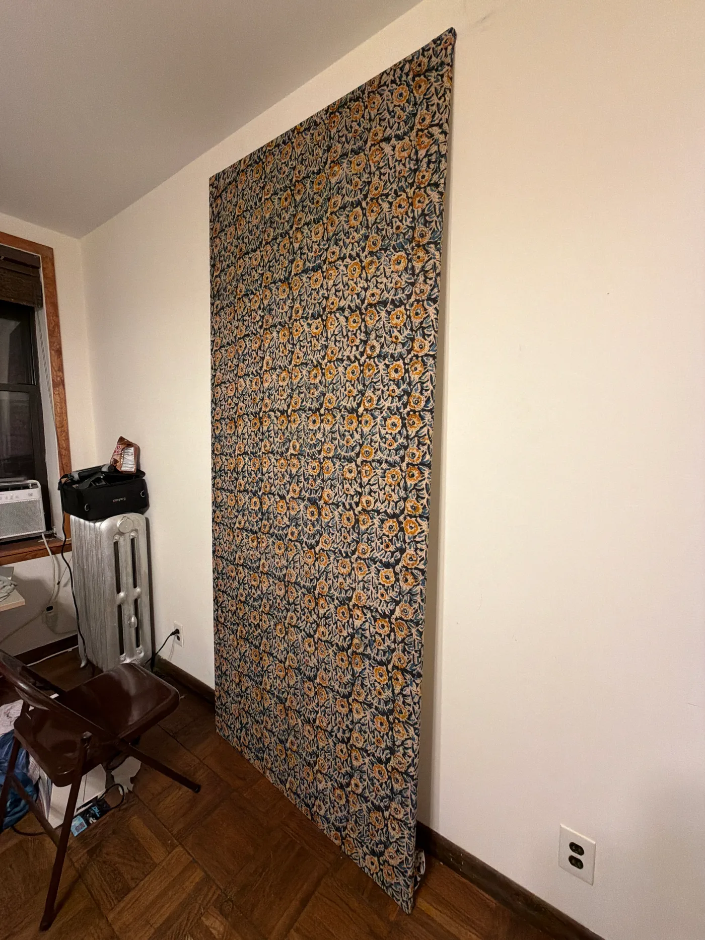 A dark floral patterned textile hanging on a white wall in a room