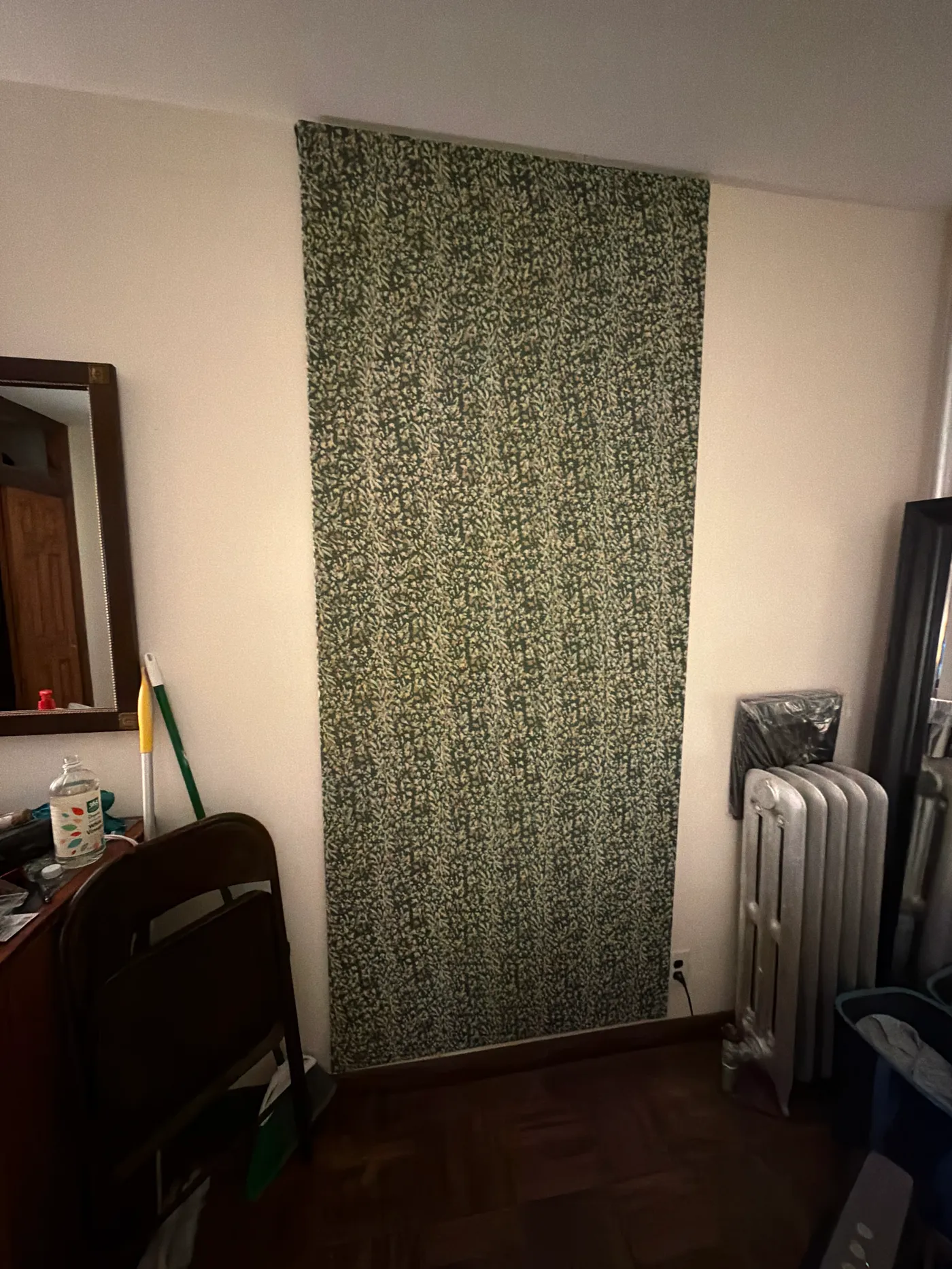 A green patterned textile hanging on a wall beside a radiator