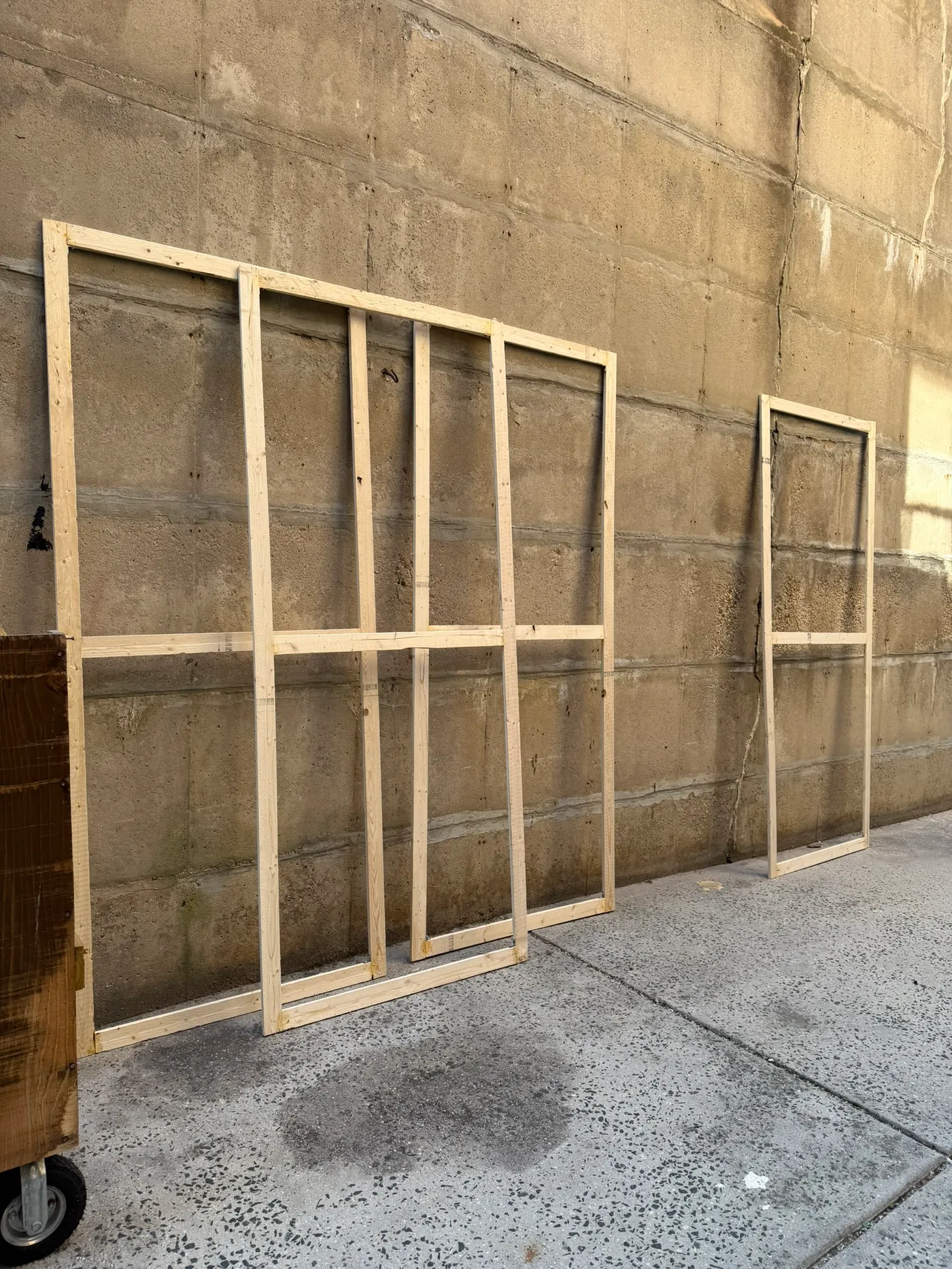 Unfinished wooden frames leaning against a concrete wall outdoors